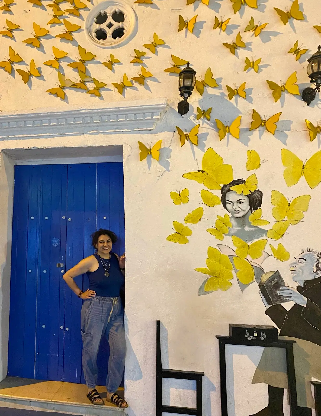 Reyah standing in front of a blue door, next to a wall covered in butterflies